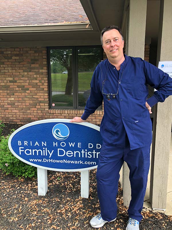 The image shows a person standing outside a building with a sign that reads  Brian Howell DDS Family Dentist.