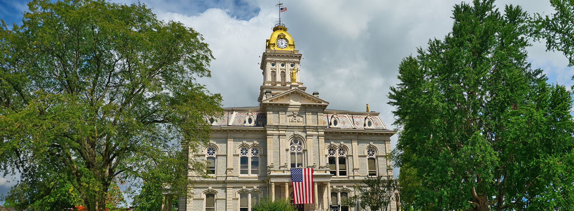 The image shows a large building with a clock tower, likely a courthouse, surrounded by trees against a clear sky.