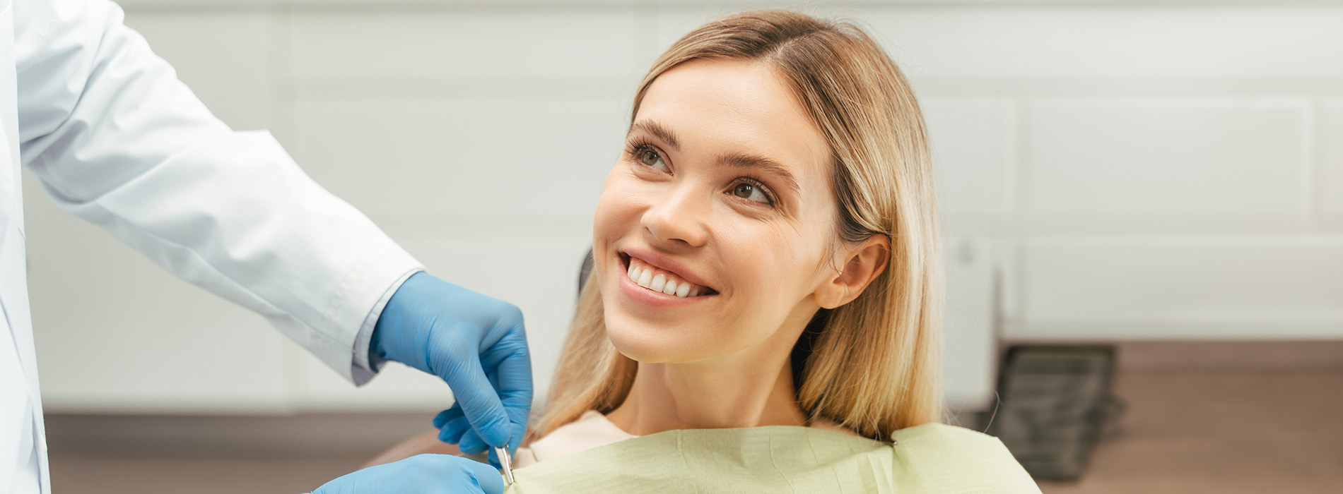 The image shows a woman seated with her eyes closed, receiving dental care from a professional who appears to be performing a cleaning or examination procedure.