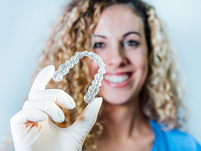 A woman with a large smile holds up a clear plastic container filled with white pearl-like beads.