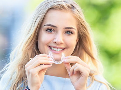 The image shows a young woman smiling at the camera while holding a dental impression tray with her teeth inside.