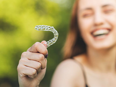 The image shows a person holding up a clear plastic object resembling a toothbrush with bristles, smiling at the camera.