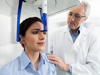 A medical professional stands beside a patient who is seated in a dental chair, with a device on the patient s head, possibly for a dental examination or treatment.